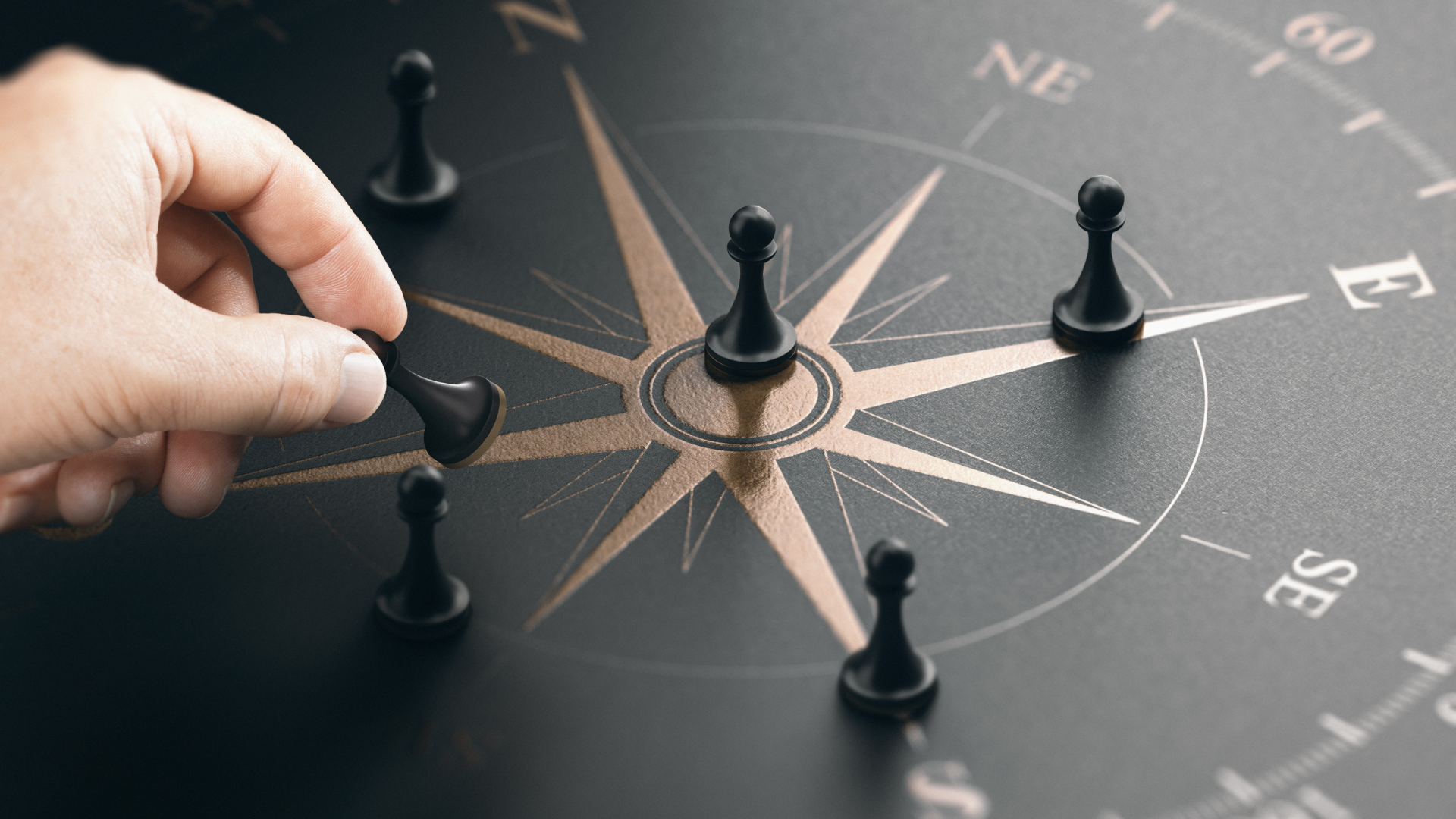 Hand bewegt eine schwarze Spielfigur auf einem Kompass, umgeben von weiteren Figuren, als Symbol für Führung, Orientierung und unterschiedliche Richtungen im Team.