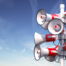 Mehrere rot-weiße Megafone auf einem Mast vor blauem Himmel – Symbol für interne Krisenkommunikation und die Herausforderung kohärenter Botschaften in Führungsteams.