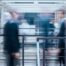 Verschwommene Silhouetten von Führungskräften in Bewegung auf einem Bürogang — symbolisch für den permanenten Wandel in Organisationen, bei dem Veränderungen einander ablösen, bevor die letzte verarbeitet ist.